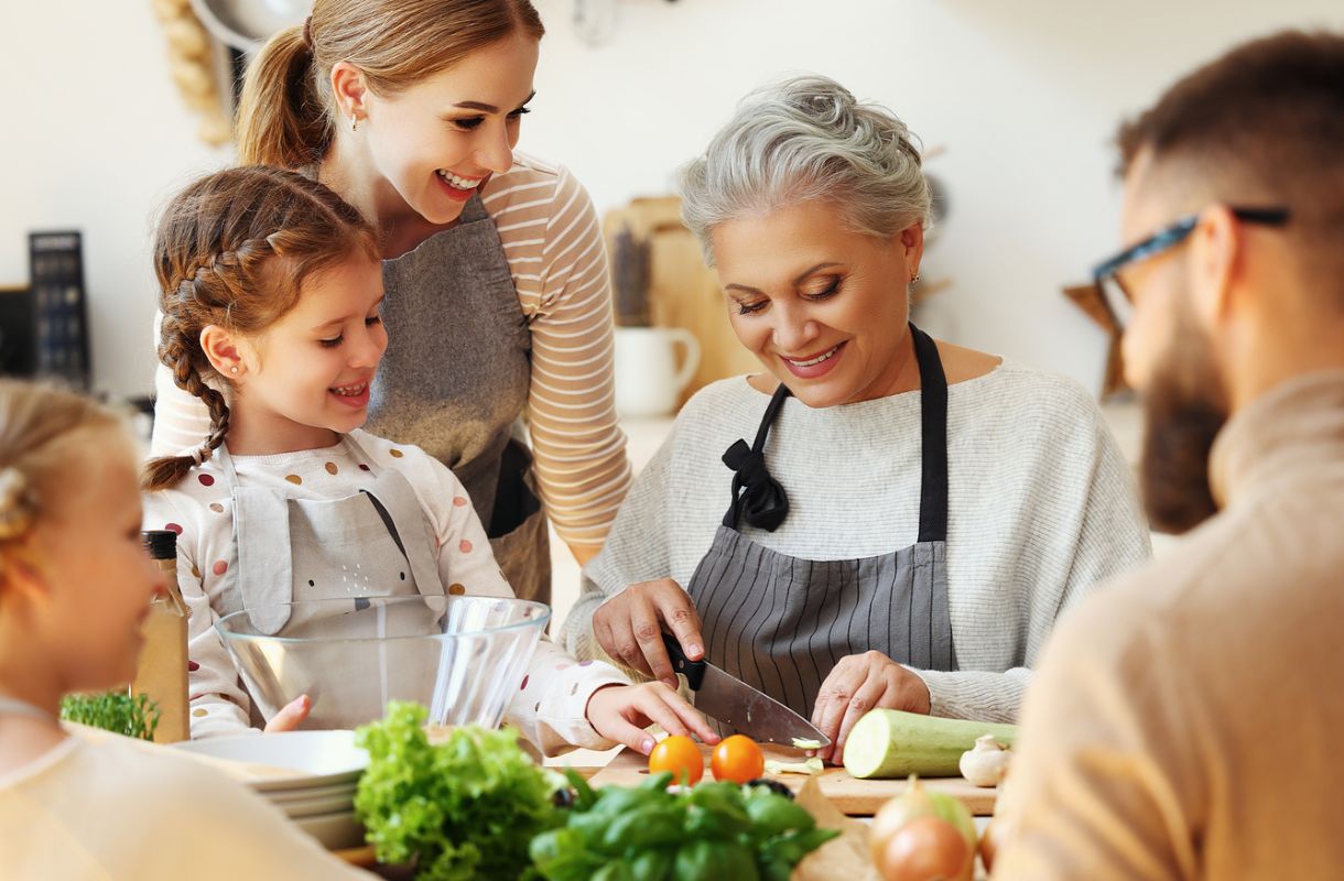 Smiling multi-generation family at a table, the matriarch chopping vegetables