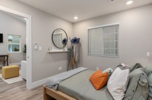 Welcoming rental or AirBNB casita bedroom with wood frame bed and neutral bedding with an orange pillow