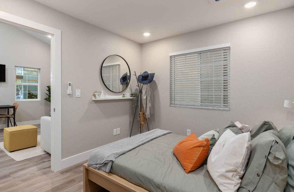 Welcoming rental or AirBNB casita bedroom with wood frame bed and neutral bedding with an orange pillow