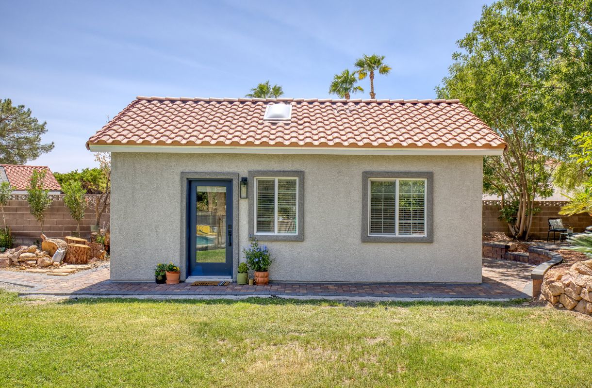 A small home with trees behind it and some potted flowers near the front door.